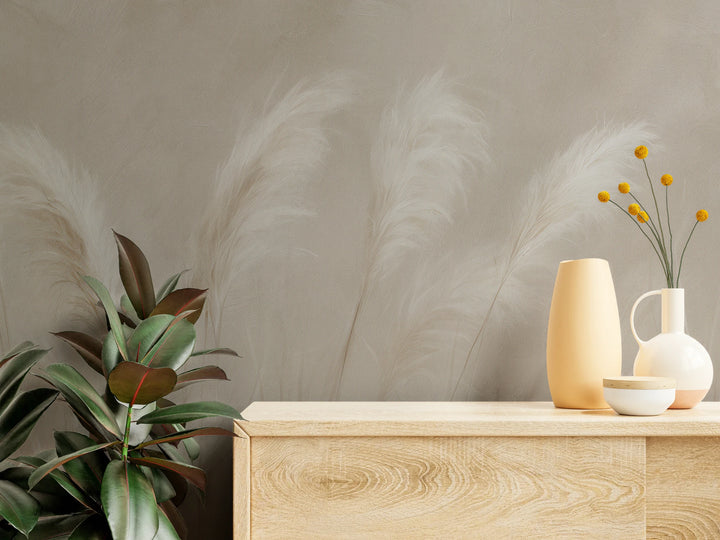 BECALMED en gros plan – plumets de pampa derrière une commode en bois clair avec vases et plante verte