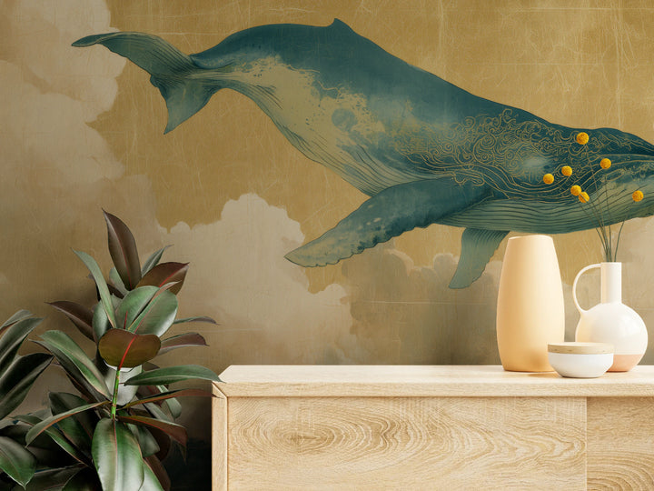FLOATING WORLD aus der Nähe: Schwanzflosse und Rumpf des Wals mit goldenem Spiralornament über heller Kommode mit Vasen